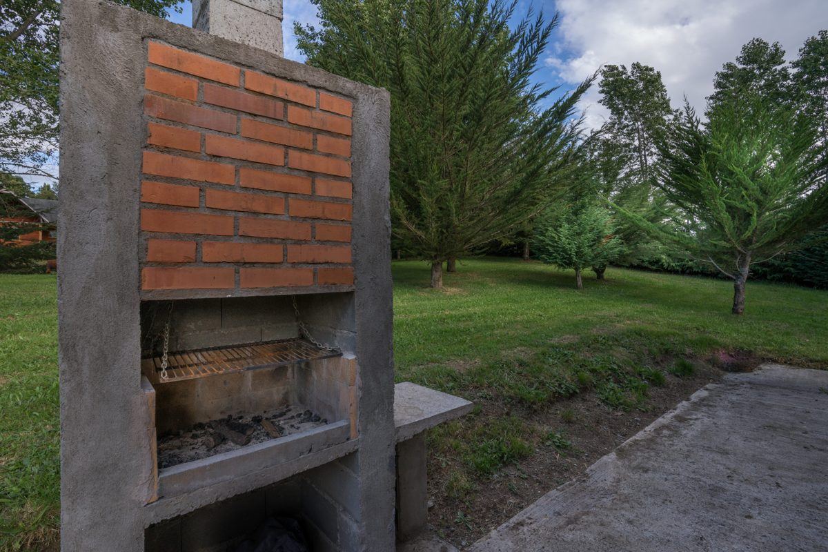 Parrilla de ladrillo en el jardín de las cabañas, rodeada de árboles