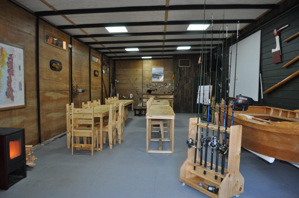 Sala de clases de la Escuela de Pesca, con mesas de madera, estufa, cañas y un bote de madera