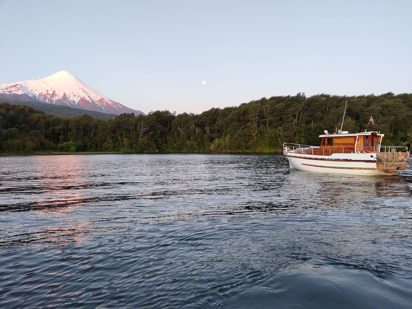 Yate Lithium fondeado al atardecer, con el volcán Osorno nevado y la luna llena sobre el bosque